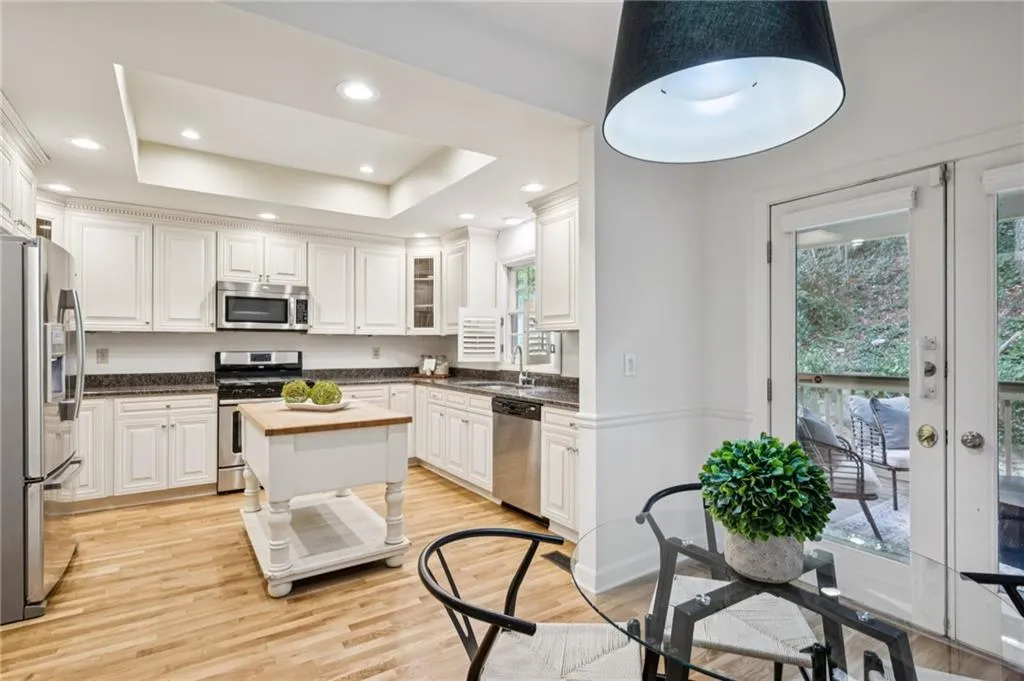 Kitchen with appliances with stainless steel finishes, light wood finished floors, white cabinetry, recessed lighting, and a tray ceiling
