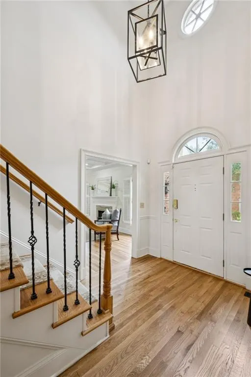 Foyer entrance with a high ceiling, light wood-style floors, a fireplace, and a chandelier