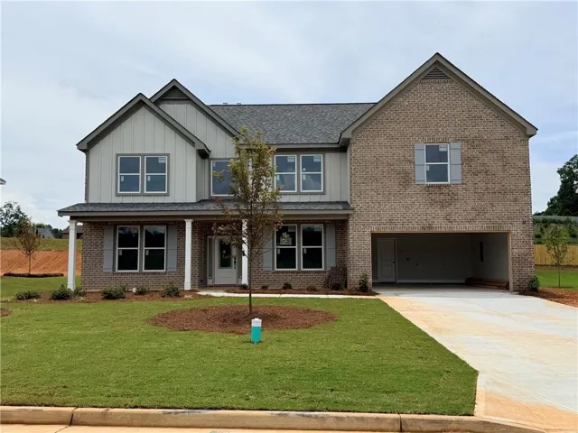Two-story residence featuring a brick and siding exterior, a covered front porch with white columns, a two-car garage, gray window shutters, and a manicured front lawn with a young tree