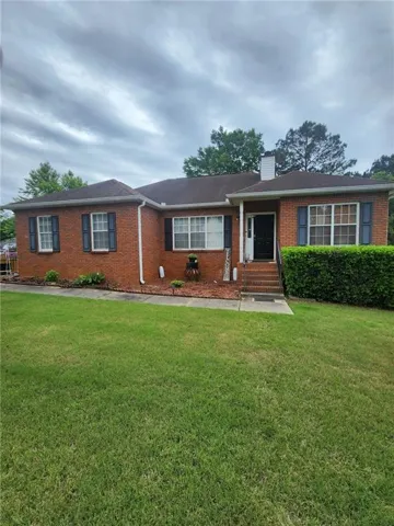 Brick exterior with dark shutters, a covered entry, and a front yard with established landscaping