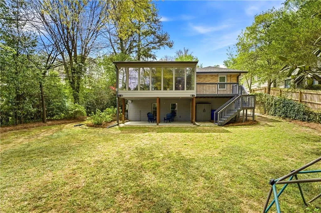 Private backyard with mature trees and open green space. Elevated deck and enclosed sunroom overlook the yard, providing a strong indoor-outdoor connection.