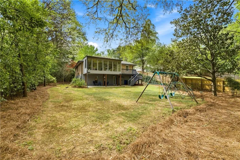 Private backyard with mature trees and open green space. Elevated deck and enclosed sunroom overlook the yard, providing a strong indoor-outdoor connection.