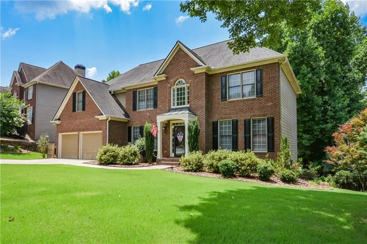 Brick facade residence featuring a front lawn, dual garage doors, a bay window with an arched transom, black louvered shutters, and established perimeter landscaping