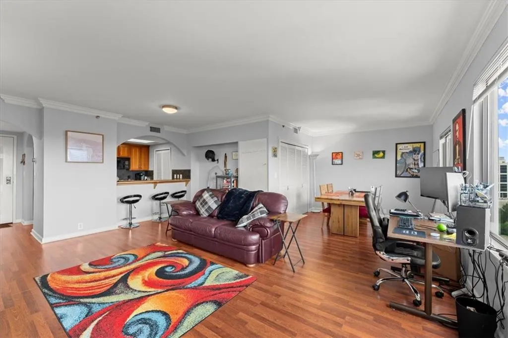 Living area with an office area, ornamental molding, wood finished floors, and arched walkways