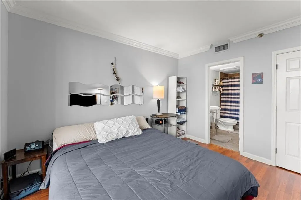 Bedroom with ornamental molding, wood finished floors, and ensuite bathroom