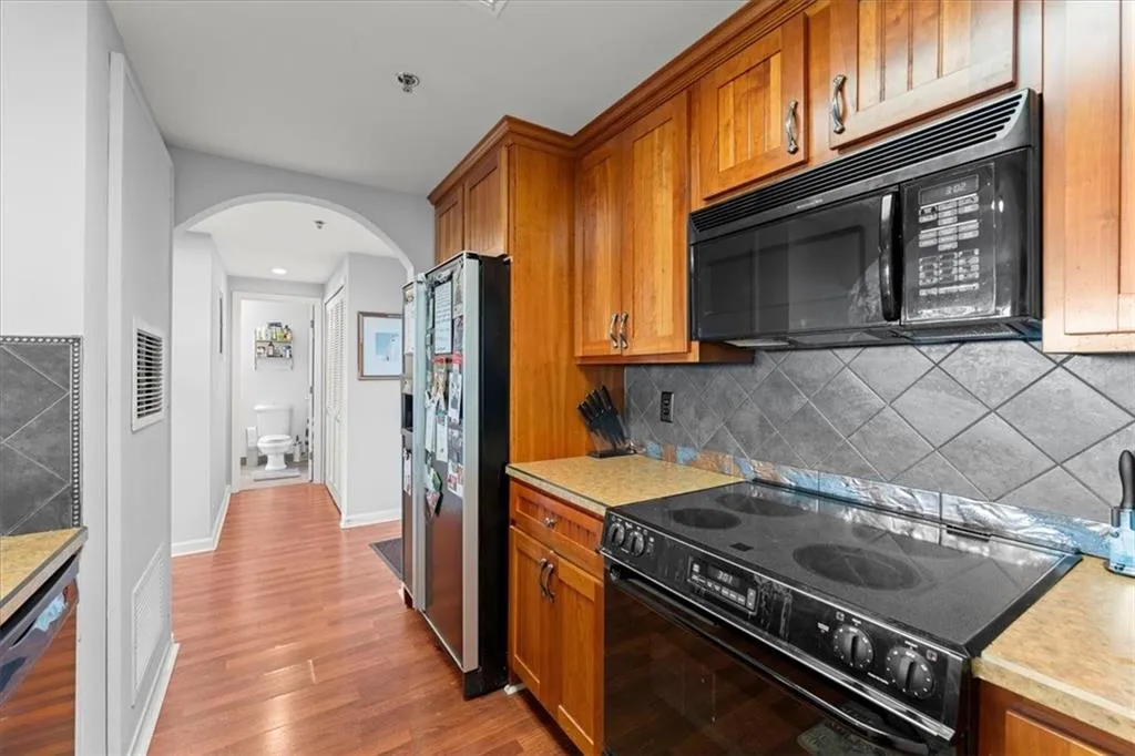 Kitchen featuring black appliances, arched walkways, brown cabinets, and light countertops