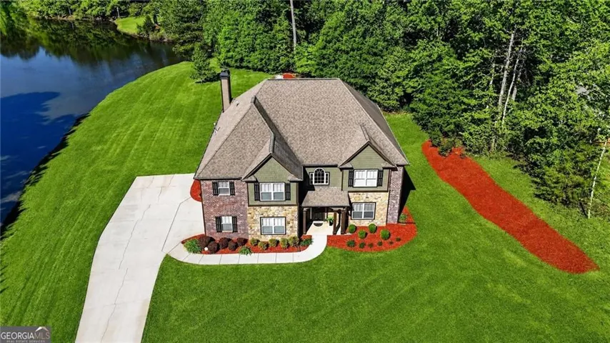 Multi-level dwelling with brick and stone facade, large driveway, mature landscaping, and waterfront access