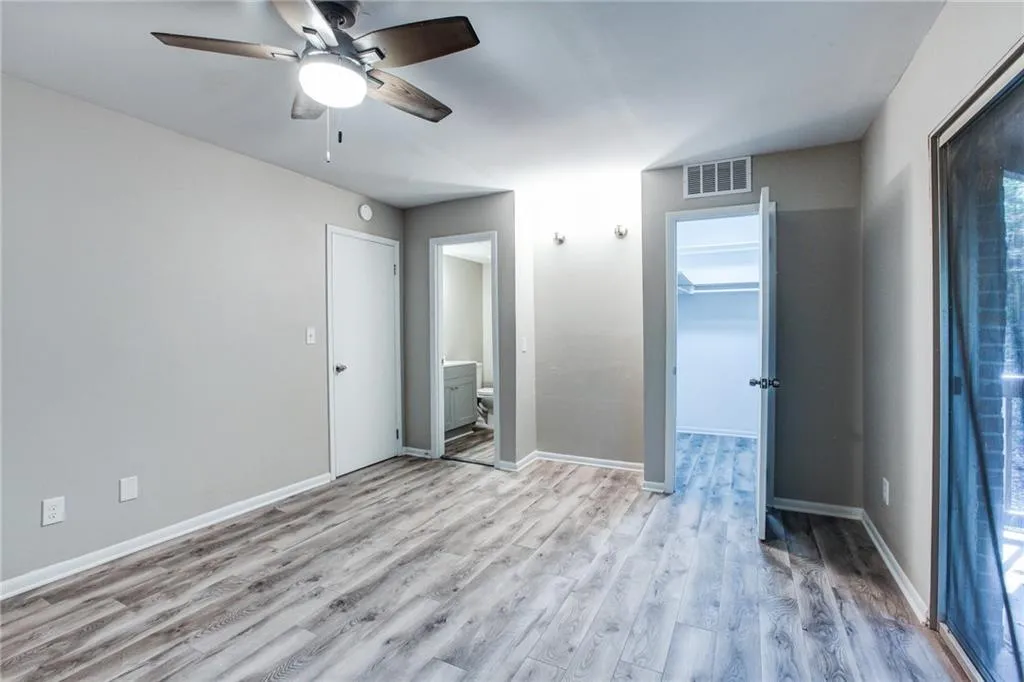 Unfurnished bedroom featuring a spacious closet, ensuite bath, light wood-type flooring, and a ceiling fan
