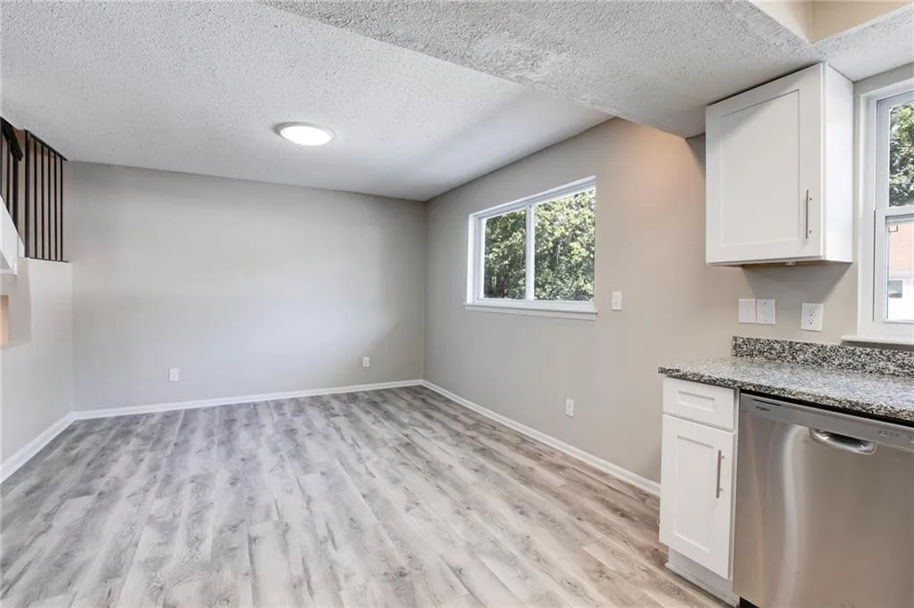 Kitchen featuring white cabinetry, stainless steel dishwasher, light stone counters, light wood-type flooring, and a textured ceiling