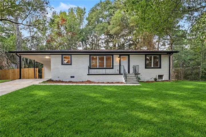 White painted brick exterior with black trim windows, a covered carport, and a concrete driveway
