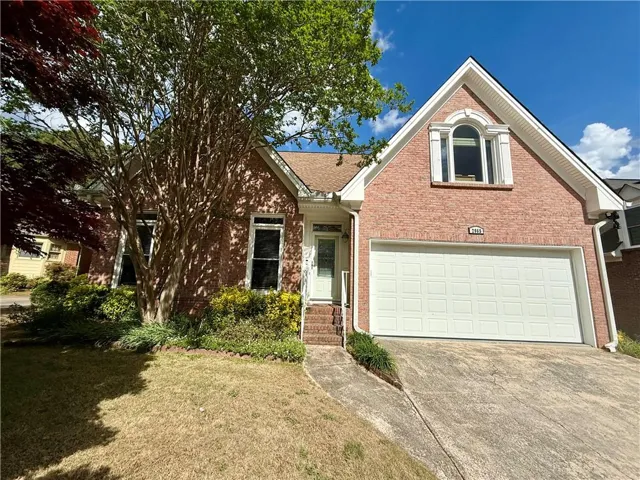 Brick exterior facade featuring a prominent arched window dormer, an attached garage with a paneled door, and a concrete driveway