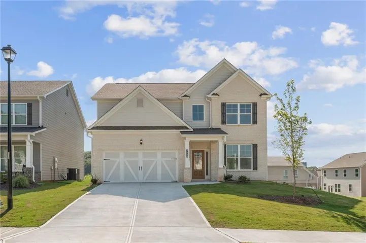 Two-story residence featuring light-colored brick and siding, a two-car garage with decorative doors, a concrete driveway, and a front entry with a warm wood-toned door