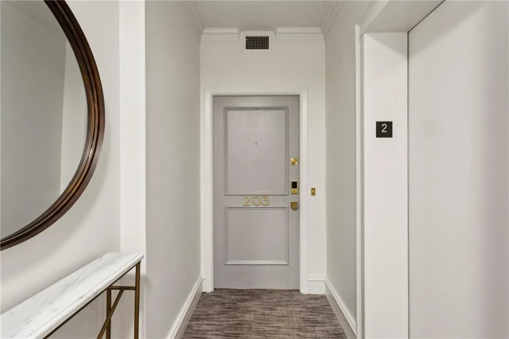 Doorway just steps from the elevator, with dark carpet, baseboards, and ornamental molding