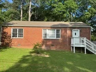 Brick exterior with a gabled roofline, multiple windows, and an elevated entry with a white deck and staircase
