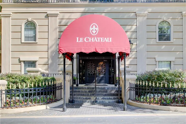Grand entryway featuring a red awning, ornate double doors, and a decorative wrought iron fence