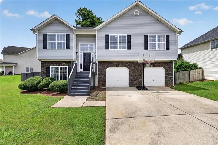 Split-level residence featuring light gray siding with dark stone accents, a dark front door with transom window, and white trim
