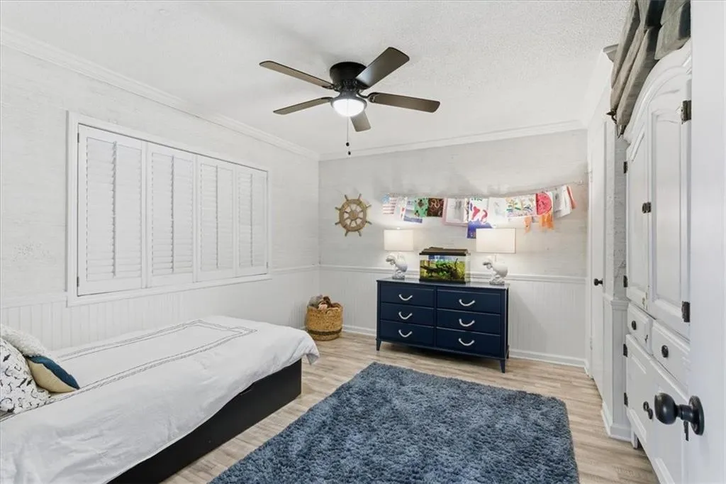 Bedroom with light wood-style floors, a wainscoted wall, a textured ceiling, ceiling fan, and crown molding