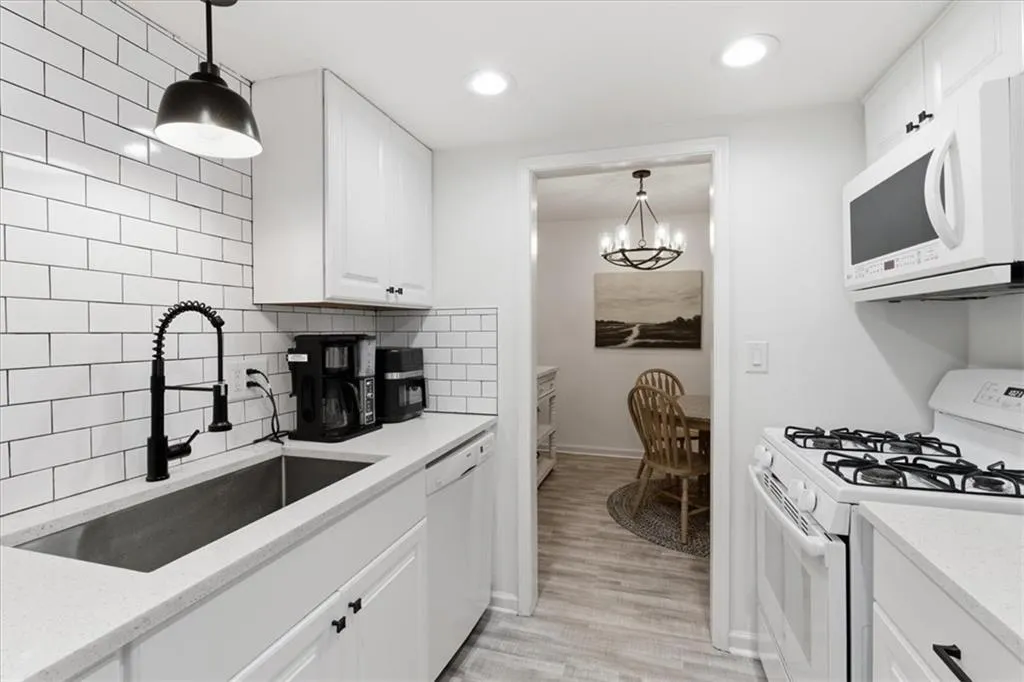 Kitchen with white appliances, hanging light fixtures, white cabinetry, light stone countertops, and a chandelier