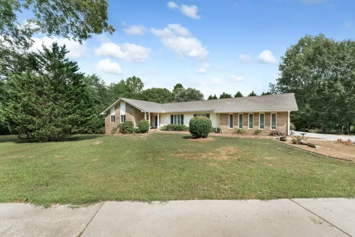 Ranch-style residence featuring a brick and white siding exterior, a gray shingle roof, and a mature treed setting