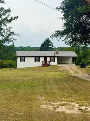 White siding exterior with dark shutters, covered front porch with steps, attached covered parking, and a stone chimney