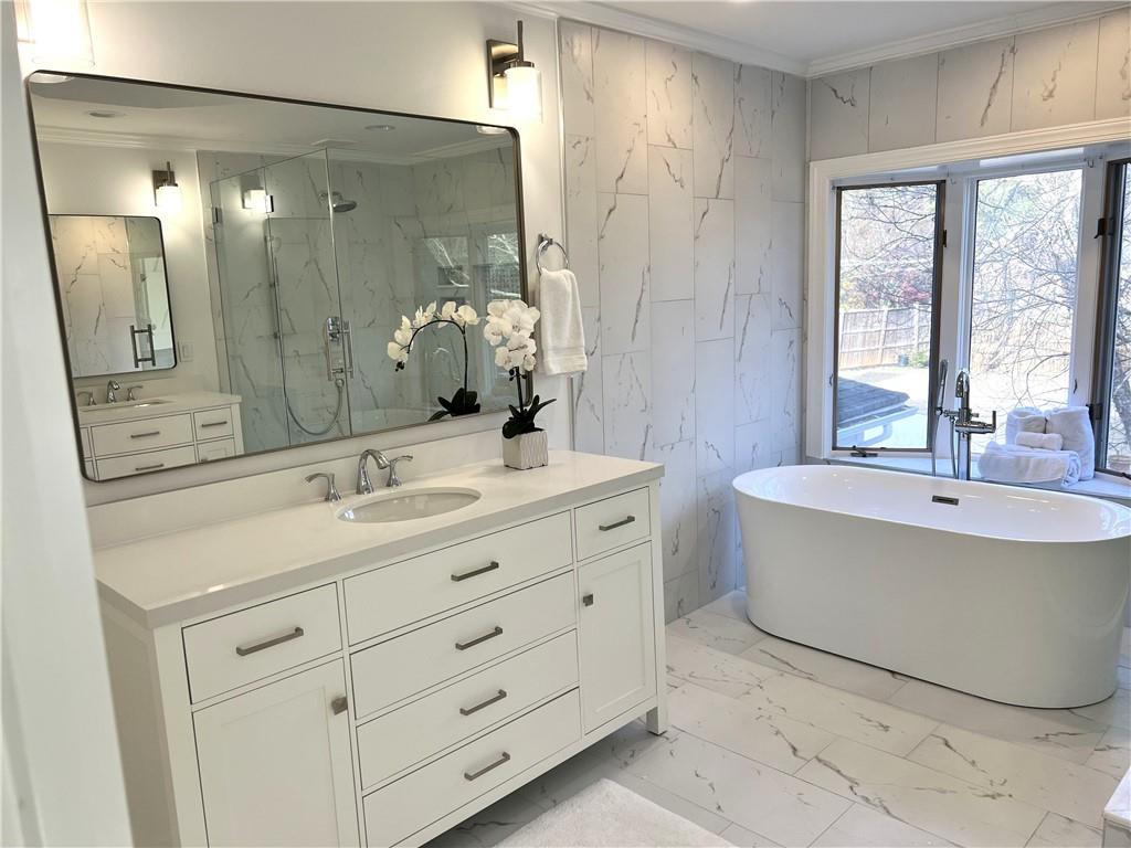 Bathroom with dual sinks, large vanity, ornamental molding, shower with separate bathtub, and tile floors