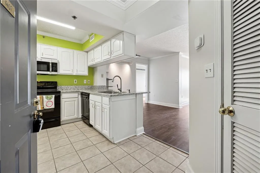 Kitchen featuring sink, light tile patterned floors, kitchen peninsula, white cabinets, and black appliances