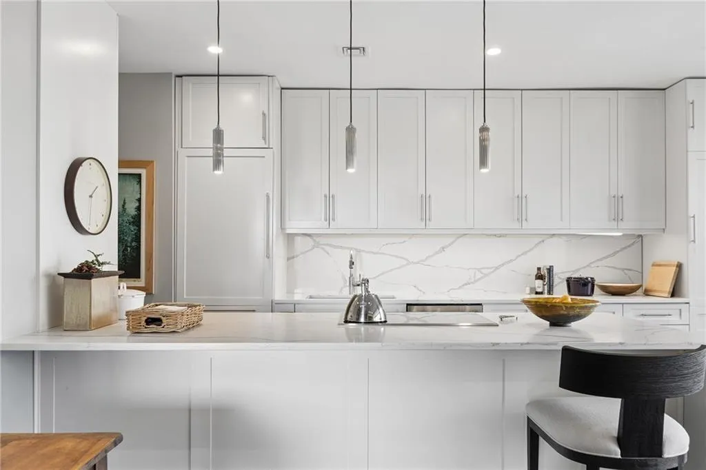 Kitchen with light stone countertops, white cabinets, decorative backsplash, a kitchen breakfast bar, and decorative light fixtures