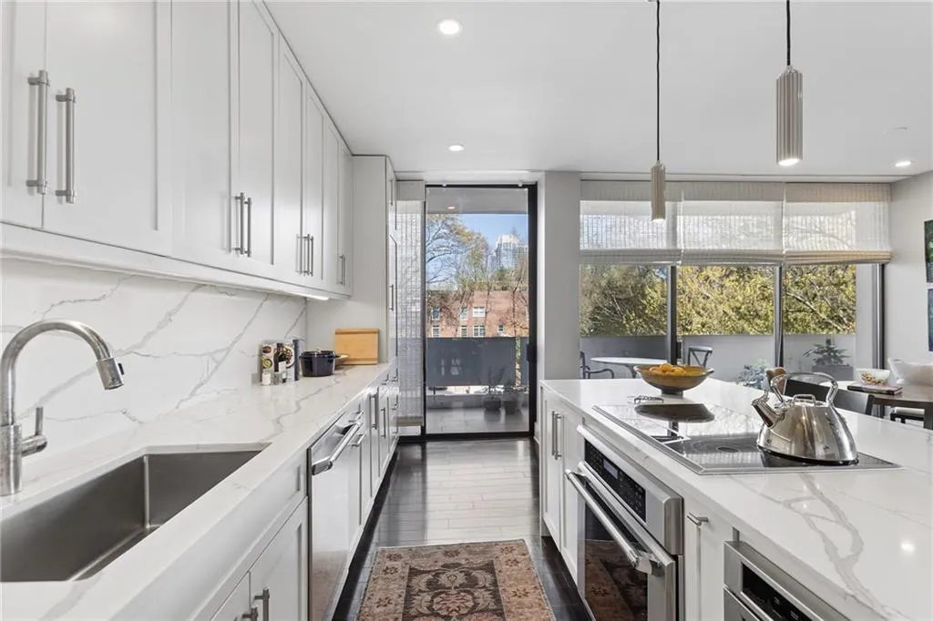 Kitchen with stainless steel appliances, light stone counters, white cabinetry, and decorative light fixtures