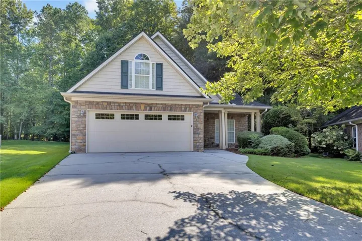 Stone facade with siding accents, arched window, two-car garage, covered entry, and mature landscaping