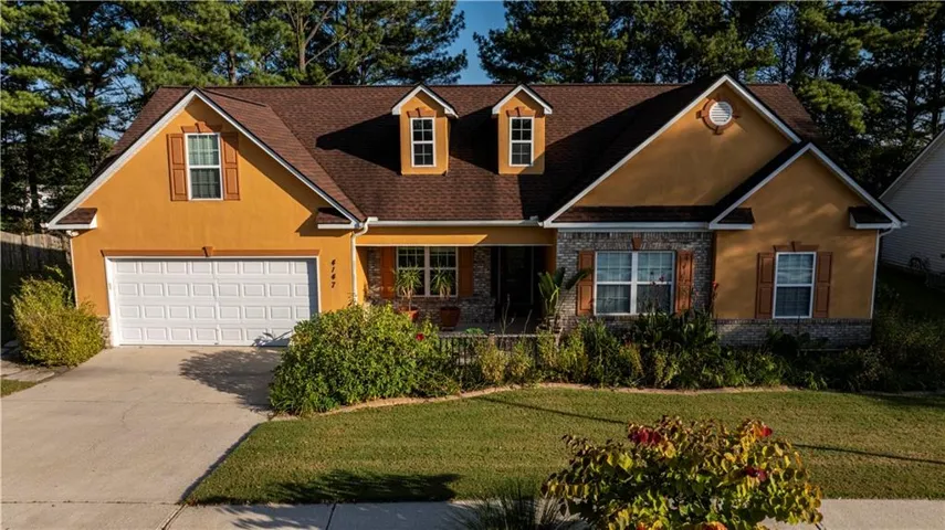 Stucco exterior with stone accenting, prominent dormer windows, a two-car garage, and a covered porch entry