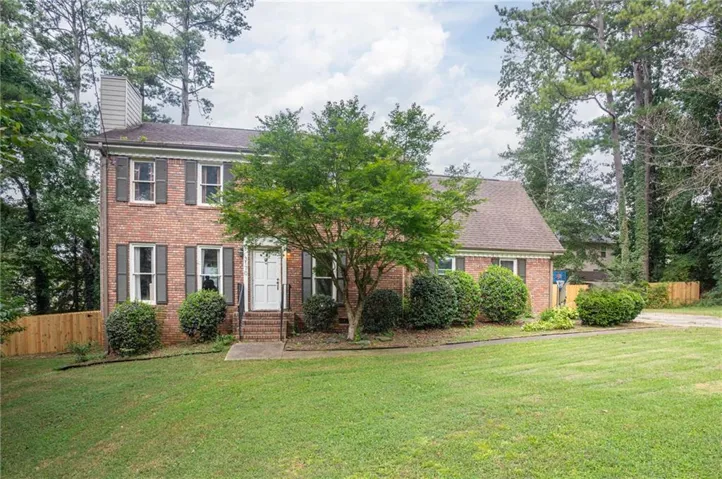 Traditional brick residence featuring a prominent two-story facade with white door, dark shutters, and a chimney
