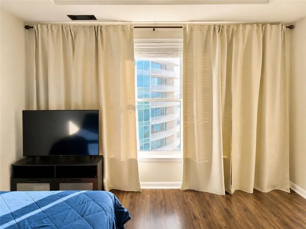 Window with light-filtering blinds, full-length drapes, and wood-finish flooring