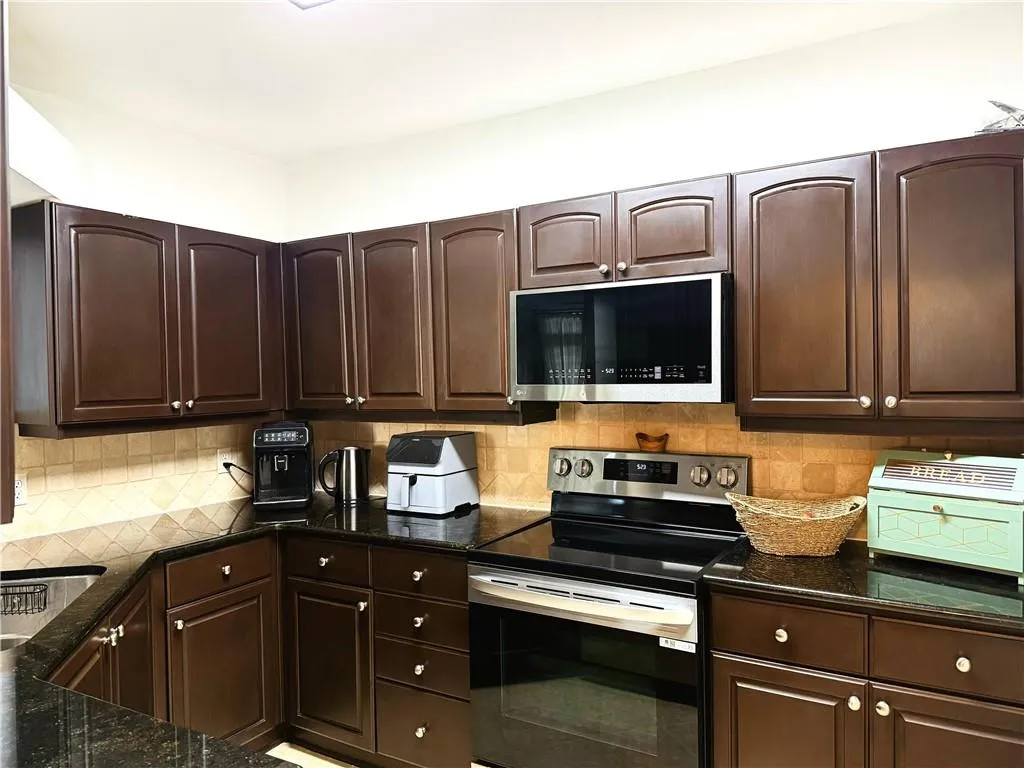 U-shaped kitchen with dark wood-finish cabinetry, black countertops, and a tile backsplash
