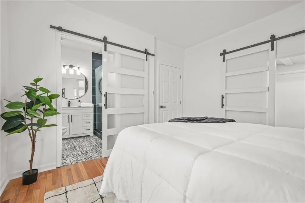 Bedroom with a barn door, wood finished floors, and connected bathroom
