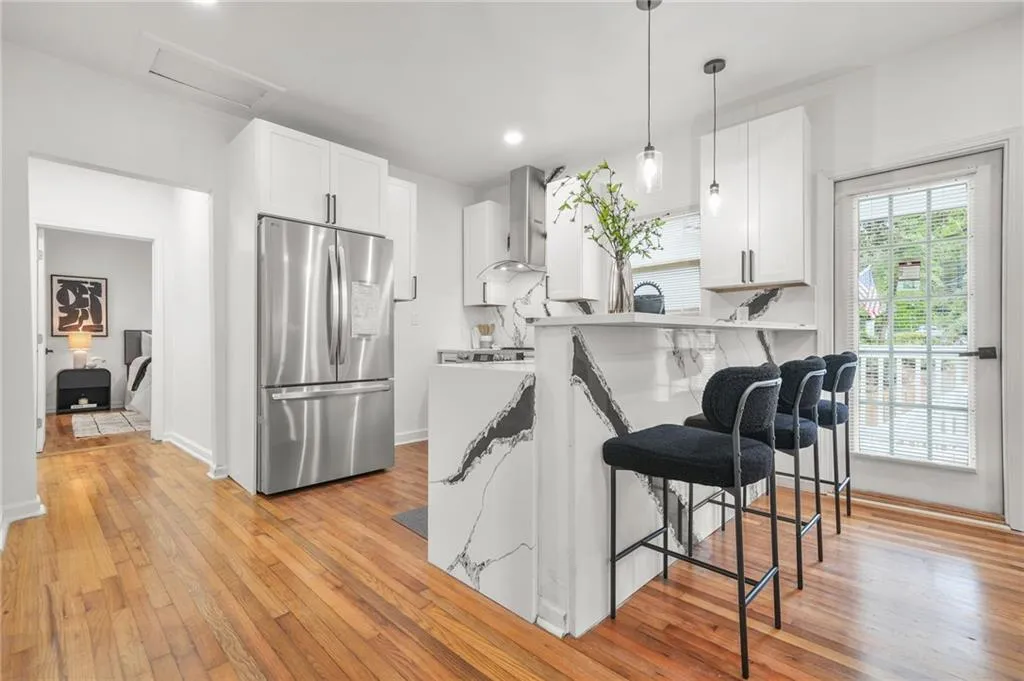 Kitchen featuring stainless steel fridge, a kitchen breakfast bar, a peninsula, white cabinets, and light wood-style floors