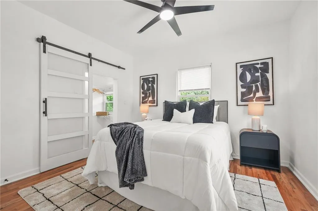 Bedroom with a barn door, wood finished floors, multiple windows, and a ceiling fan