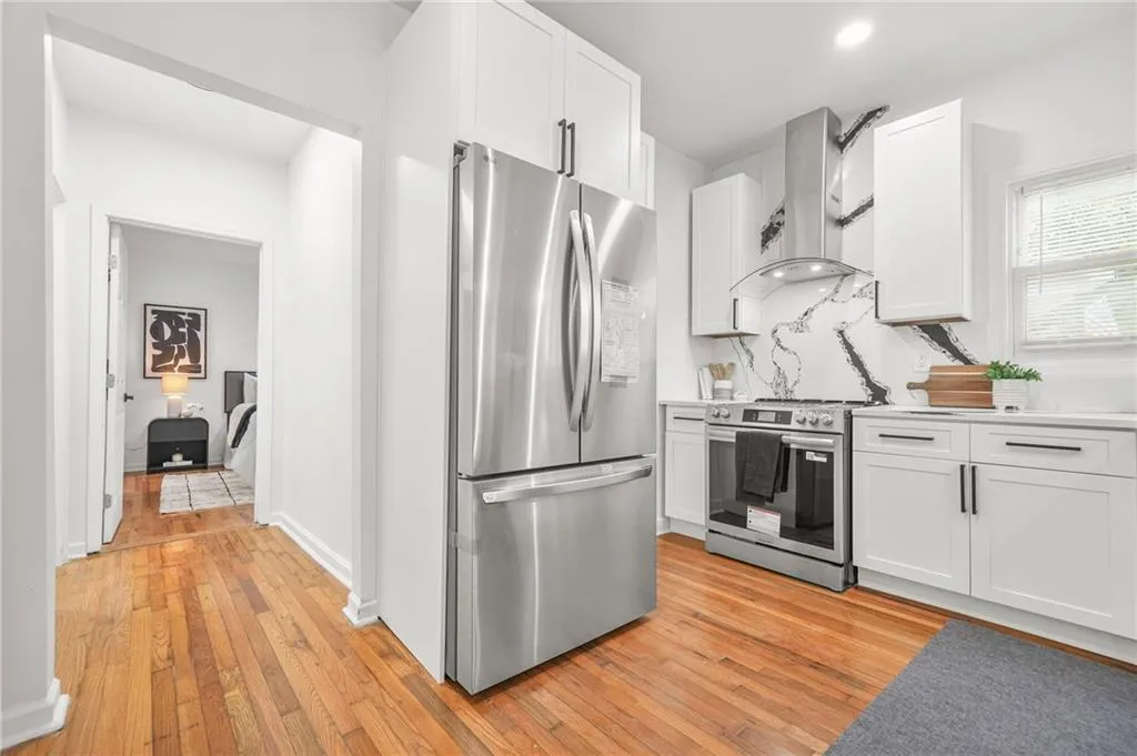 Kitchen with stainless steel appliances, wall chimney range hood, light wood finished floors, white cabinetry, and light countertops