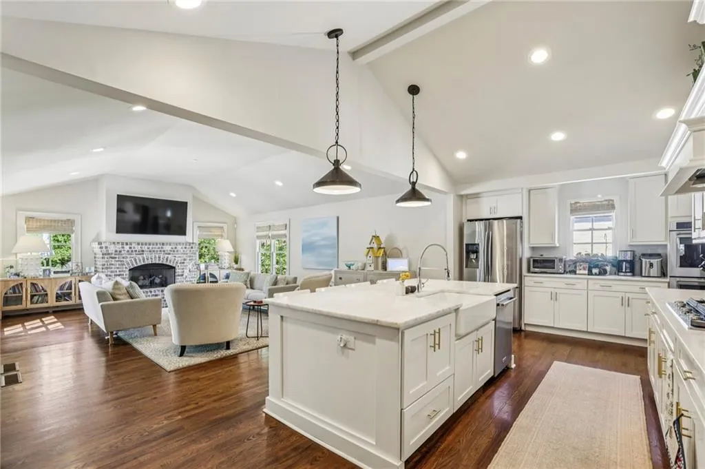Kitchen featuring white cabinetry, open floor plan, dark wood-style flooring, a brick fireplace, and decorative light fixtures
