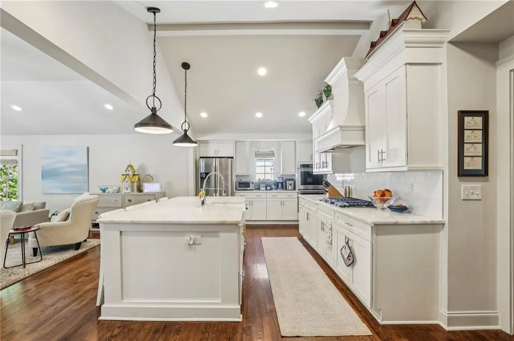 Kitchen featuring white cabinetry, light stone counters, hanging light fixtures, dark wood-type flooring, and vaulted ceiling with beams
