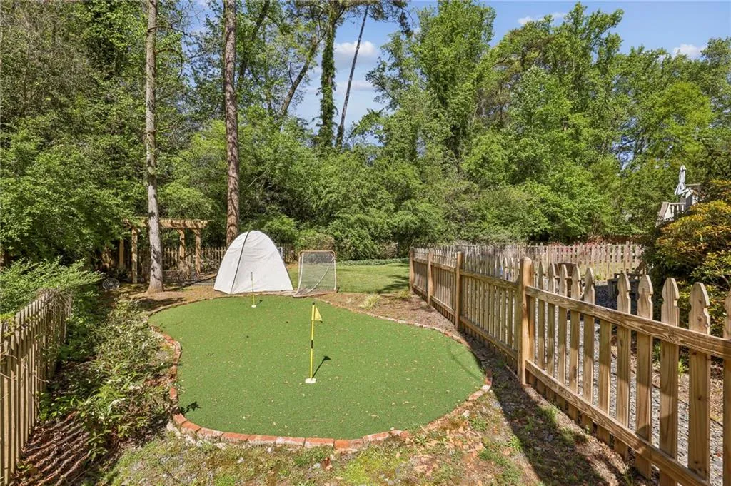 Fenced backyard with an area to practice putting and view of wooded area