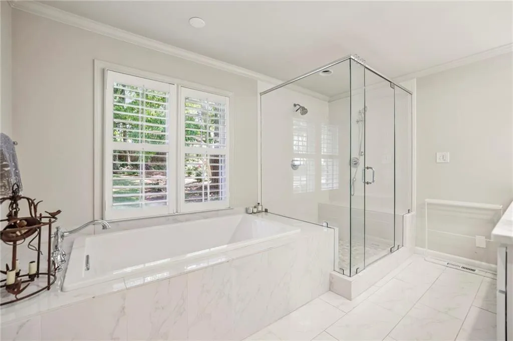 Full bathroom featuring a shower stall, ornamental molding, a garden tub, light marble finish flooring, and vanity