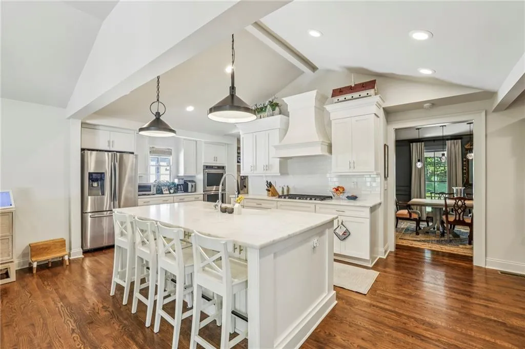 Kitchen with decorative light fixtures, stainless steel appliances, a kitchen breakfast bar, white cabinetry, and dark wood-type flooring