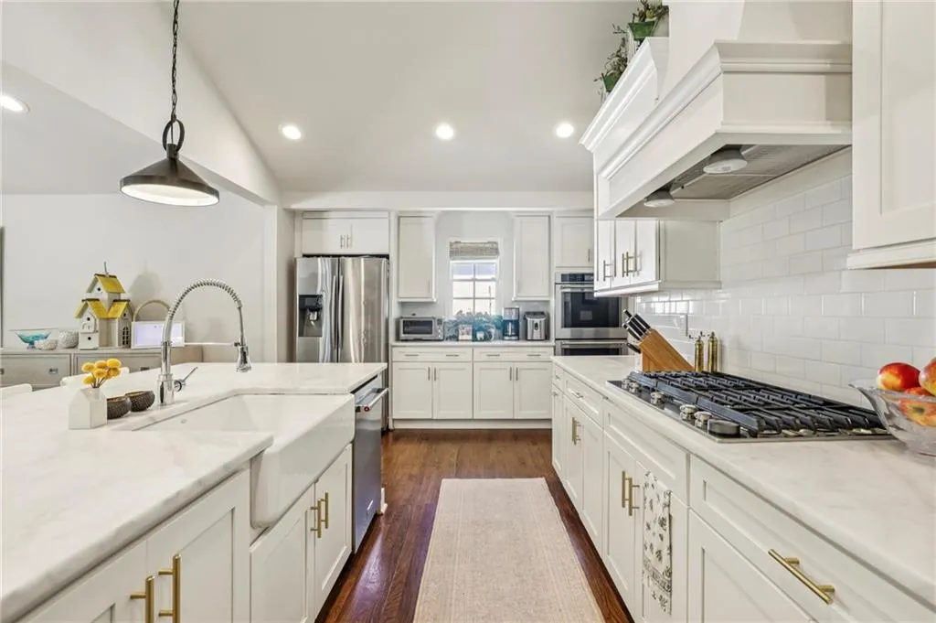 Kitchen with hanging light fixtures, white cabinetry, dark wood-style flooring, stainless steel appliances, and tasteful backsplash