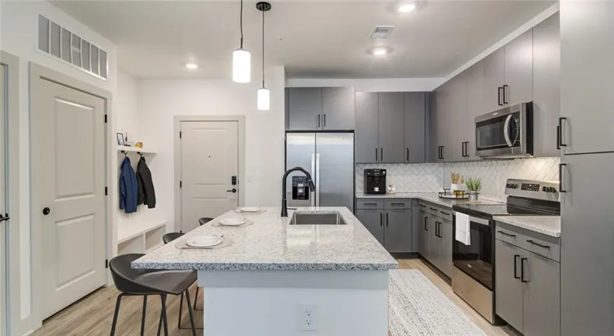 Kitchen with stainless steel appliances, hanging light fixtures, a kitchen bar, light stone countertops, and a kitchen island with sink