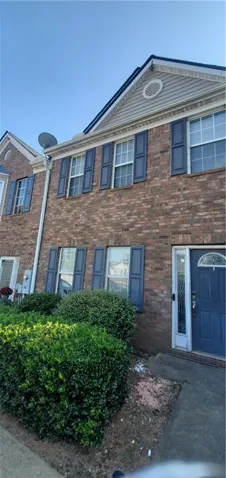 Brick townhouse exterior featuring a blue entry door with decorative glass, coordinating blue window shutters, and a front facade with a prominent gable vent