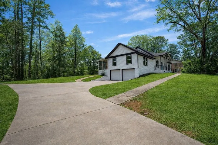 View of side of property with a garage, asphalt driveway, a lawn, and view of scattered trees