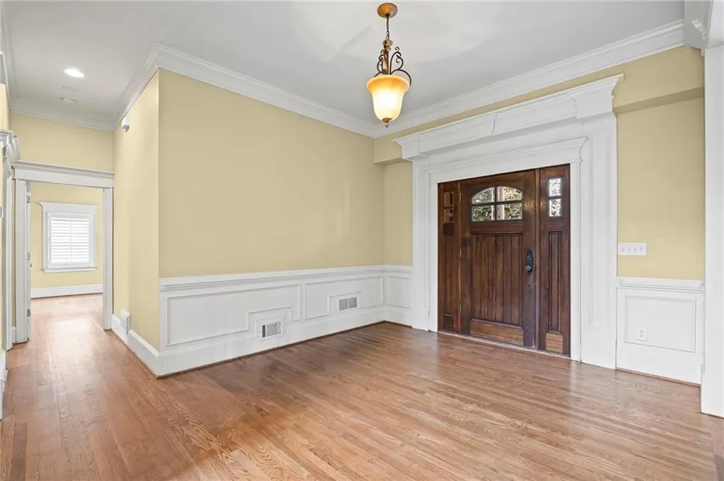 Entryway with ornamental molding, a wainscoted wall, light wood finished floors, and a decorative wall