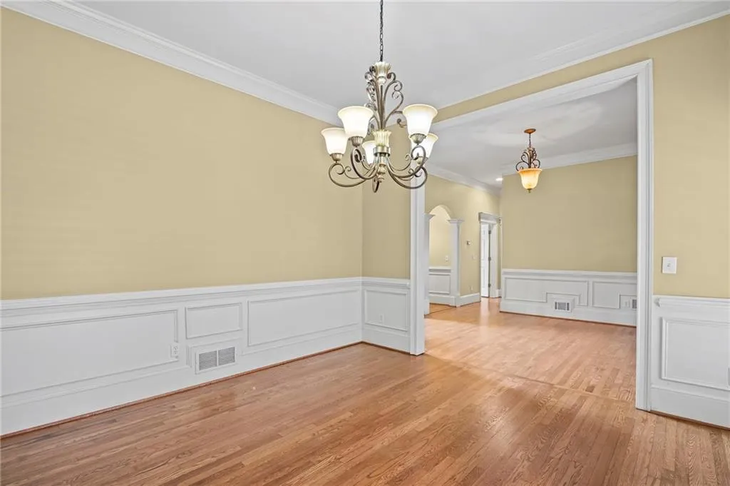 Unfurnished dining area with arched walkways, ornamental molding, a wainscoted wall, light wood-style floors, and a decorative wall