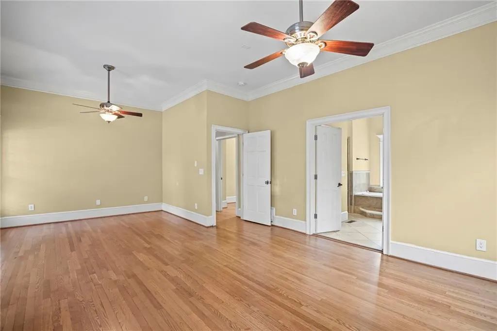 Unfurnished bedroom featuring crown molding, light wood-style floors, a ceiling fan, and ensuite bath