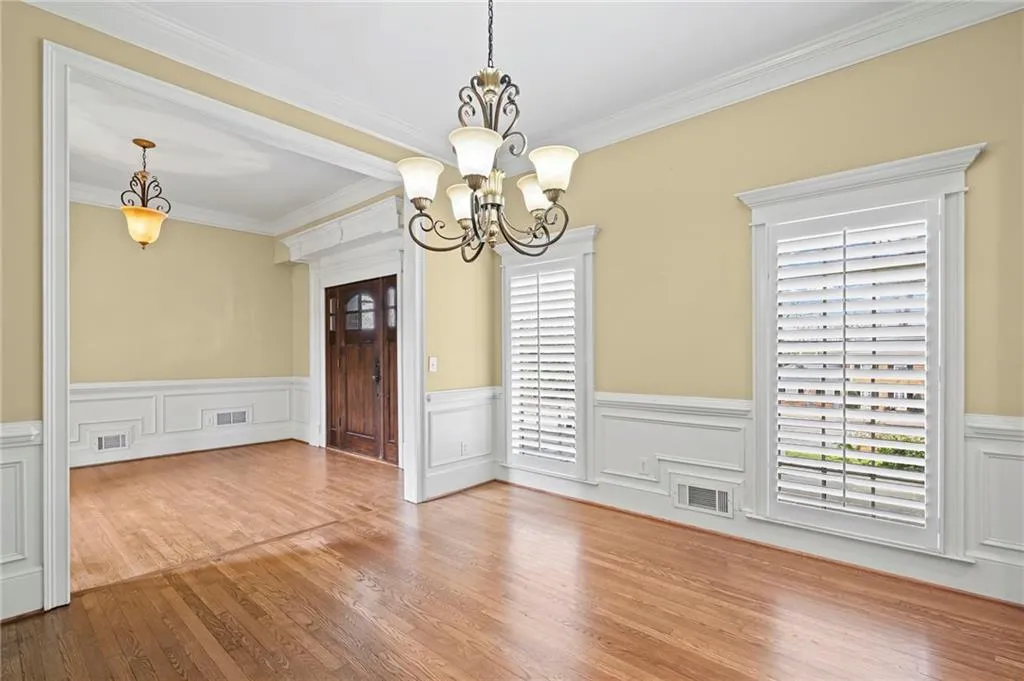 Unfurnished dining area with wainscoting, plenty of natural light, a chandelier, wood finished floors, and crown molding